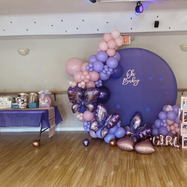 venue with gift table next to pink and purple oh baby balloon arch with girl text balloon and butterfly balloons